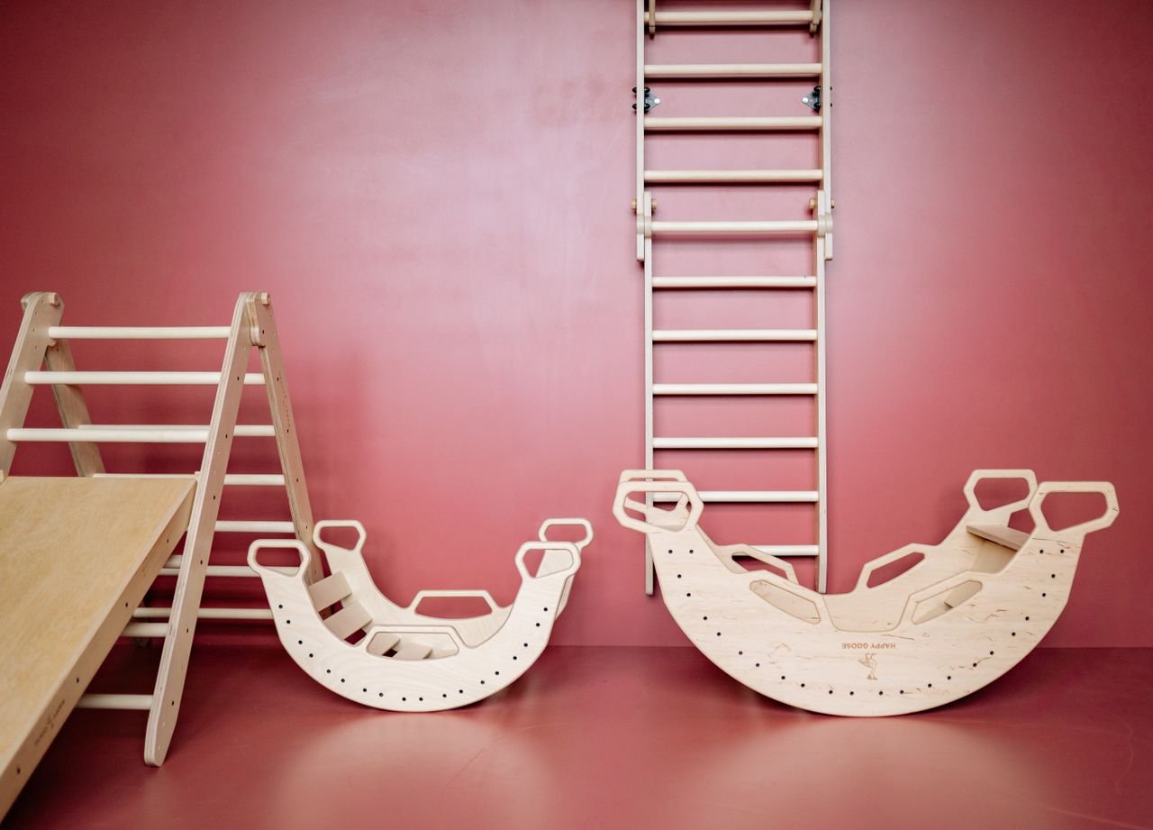 Minimalist wooden play equipment for kids indoors, set against a red background.