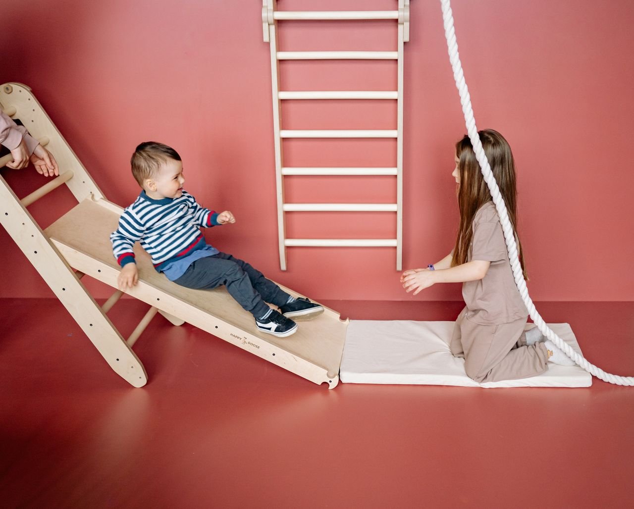 Two children having fun on a wooden slide indoors, fostering play and sibling bonding.