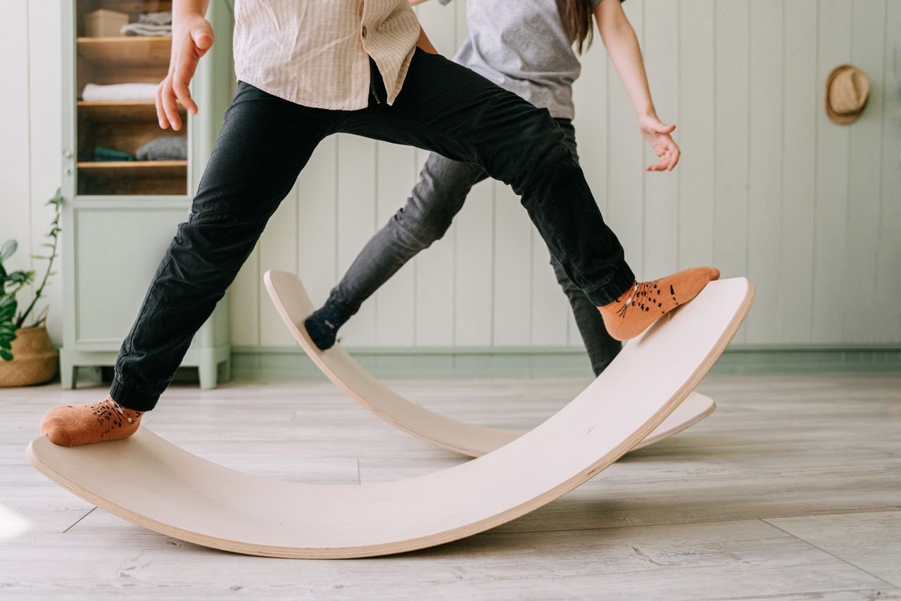Two kids playing on wooden balance boards indoors, focusing on balance and mindful activities.